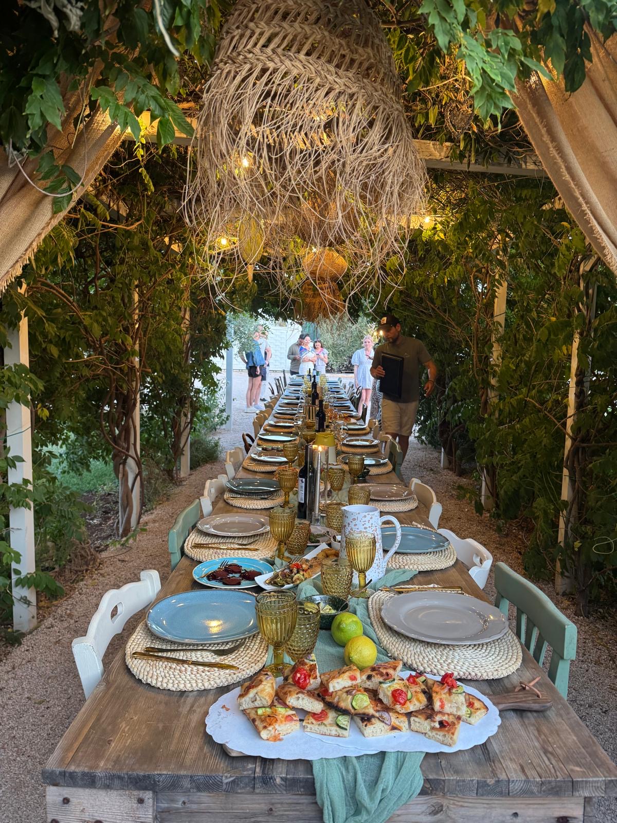 A long dinner table laid beneath a leafy pergola in Puglia