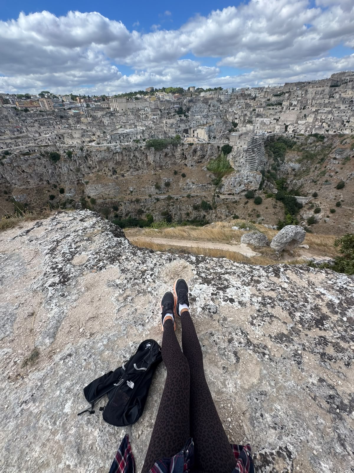 Looking across the ravine toward the Sassi of Matera, a walker's boots in the foreground