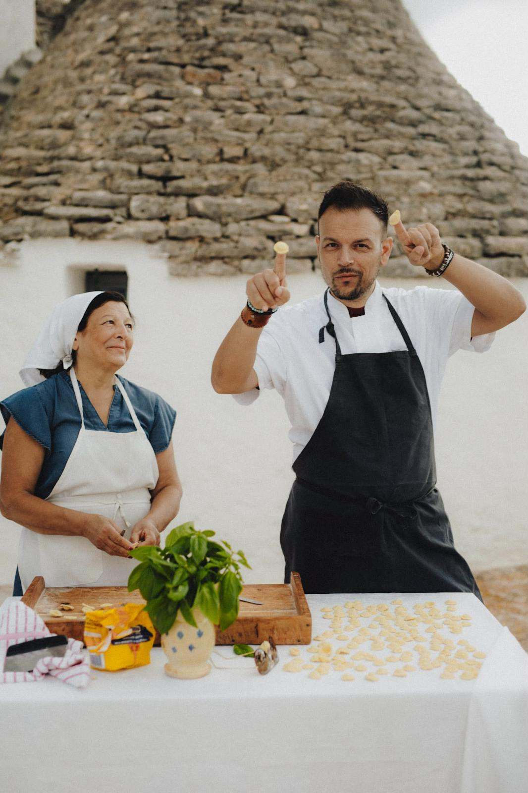 A local chef shaping orecchiette with a guest in front of a trullo