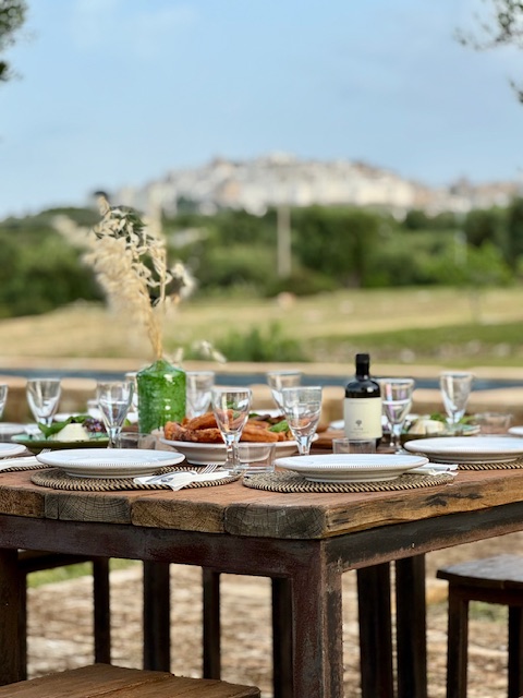 A long wooden table laid for lunch with Ostuni on the hill behind