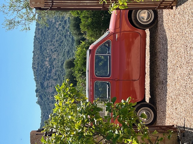 A red vintage Fiat 500 parked behind an open gate in the countryside